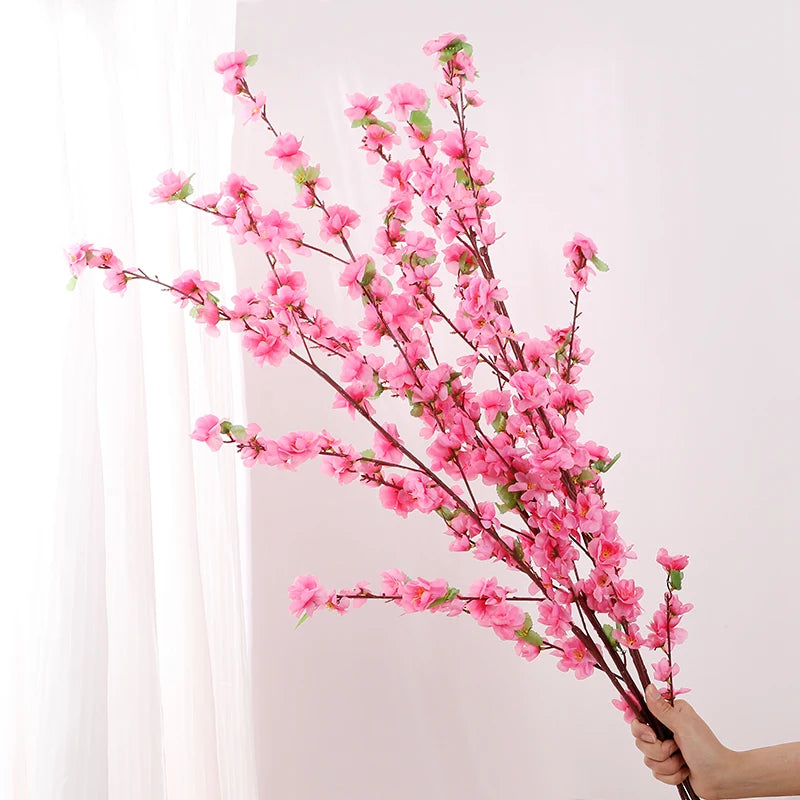 Pink artificial flower branches held by a hand against a white background