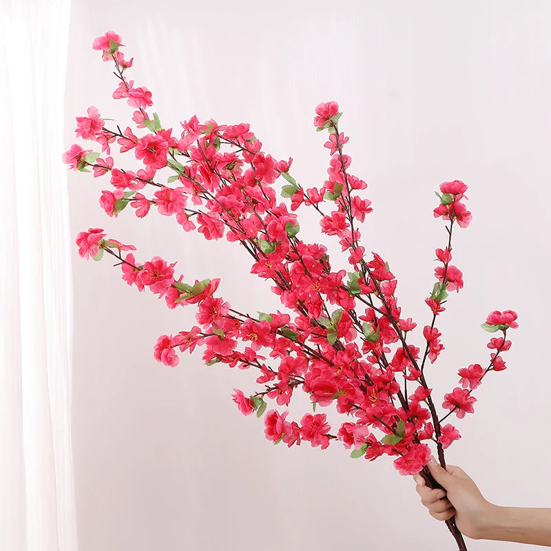 Artificial pink cherry blossom branch held by a hand against a light background