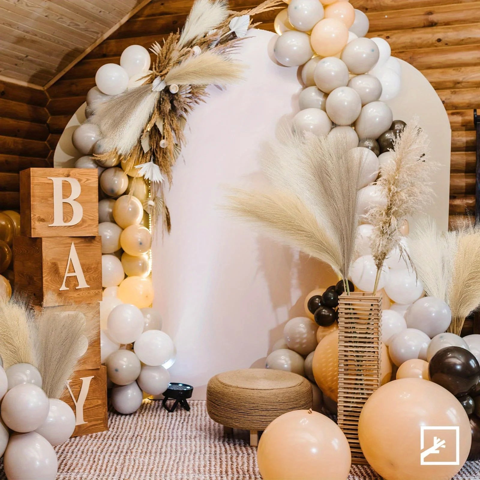 Decorative arch with balloons, pampas grass, and wooden blocks spelling 'BABY' in a rustic setting.