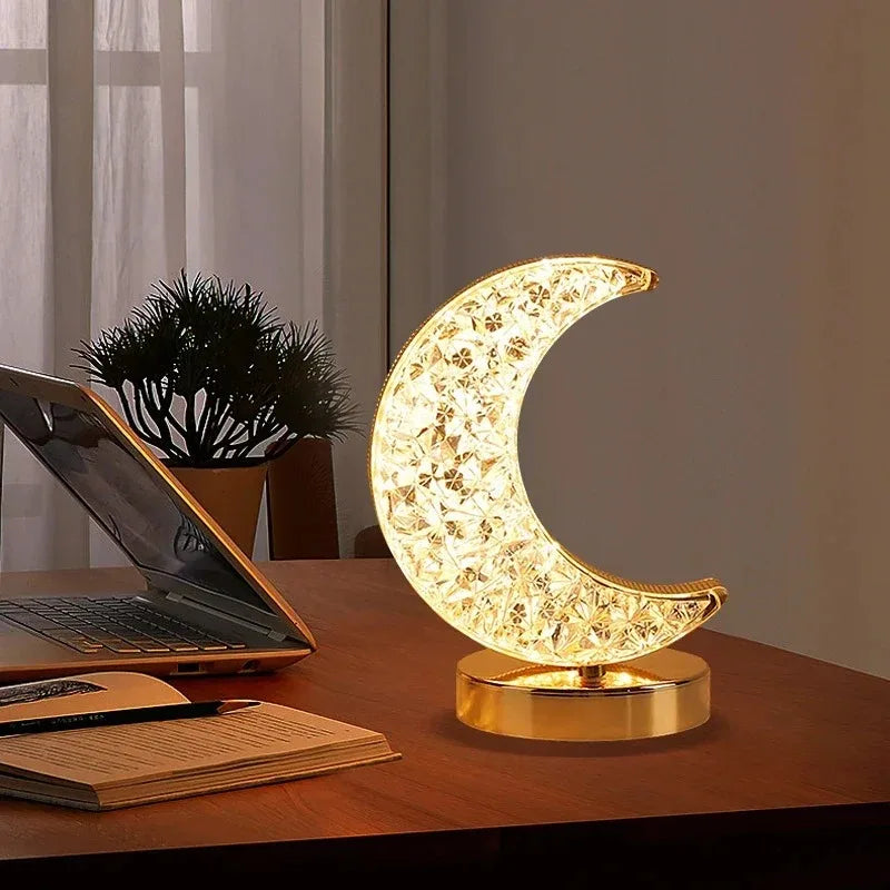 Decorative moon-shaped lamp on a desk with a laptop and notebook.