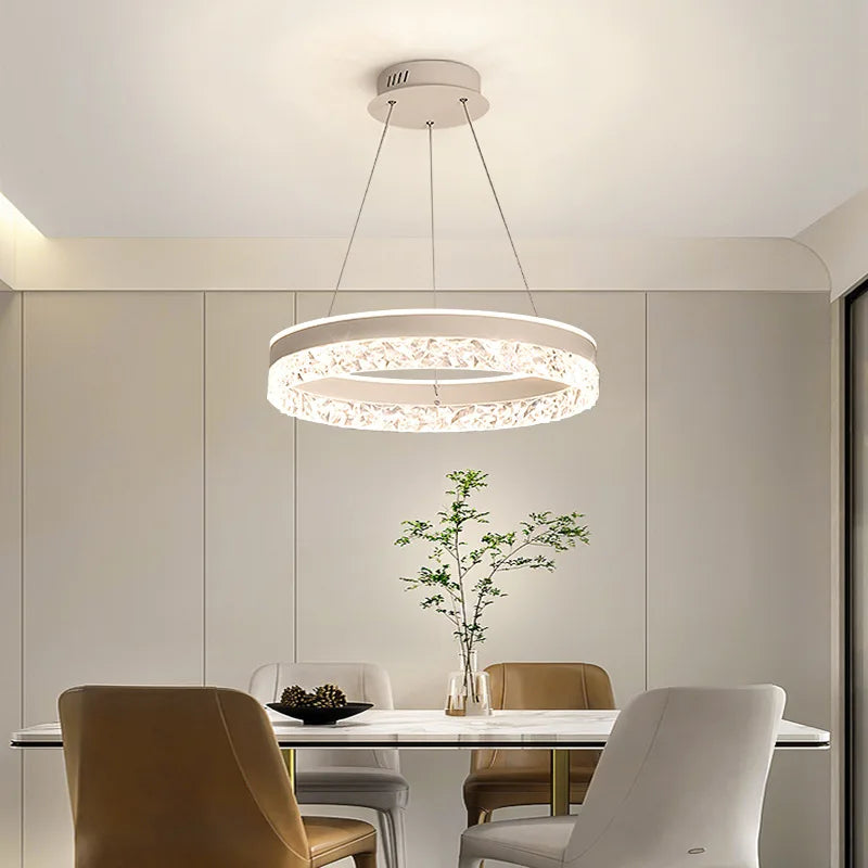 Modern chandelier hanging above a dining table with chairs in a well-lit room.